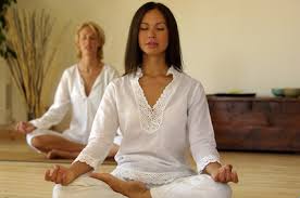 two ladies sit in meditation wearing white clothes 